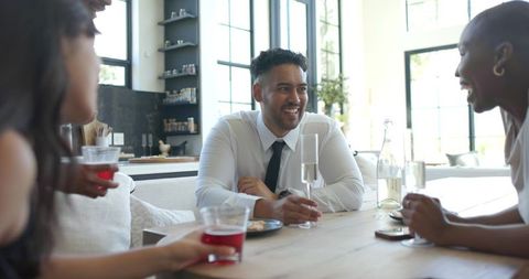 Young professional holding champagne flute chatting with colleagues at kitchen table