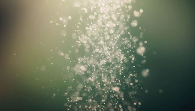 Backlit underwater light particles drifting upward with dreamy bokeh glow, soft teal tones