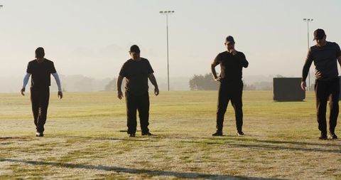 Coaching team walking across dewy field at sunrise in matching dark training gear
