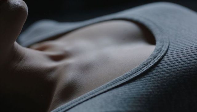 Low-key closeup of female collarbone and neck in grey ribbed tank highlighting skin texture