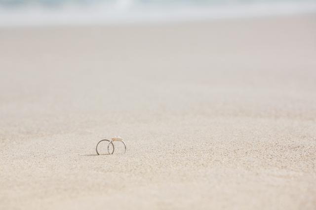 Wedding rings placed on sandy beach, symbolizing love and commitment. Ideal for use in wedding invitations, romantic getaway promotions, engagement announcements, and beach-themed wedding decor.