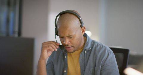 African American man adjusting headset while working at desk with monitor, focused