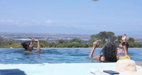 Women chatting and playing in infinity pool overlooking city and mountain panorama