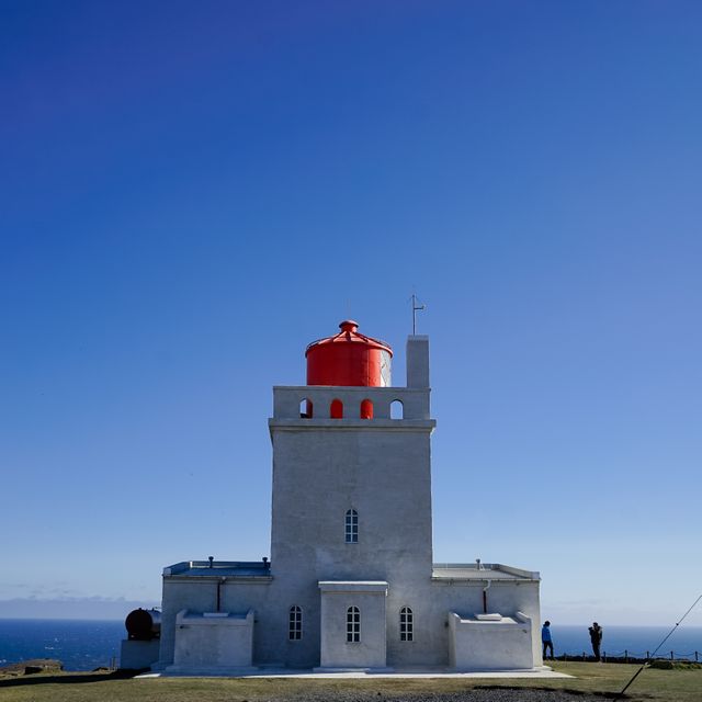 Majestic lighthouse with distinct red roof against bright blue sky, suitable for travel, coastal guides, and inspirational posters. Highlights architectural beauty and navigational significance.