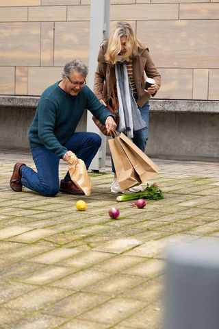 Senior man kneeling while couple picking up spilled groceries from urban pavement