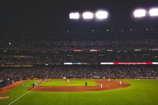 Nighttime baseball game with packed stadium full of spectators under bright lights. Baseball field with players visible in action. Ideal for topics on sports events, major league baseball, live events, outdoor activities, and competitive sports.