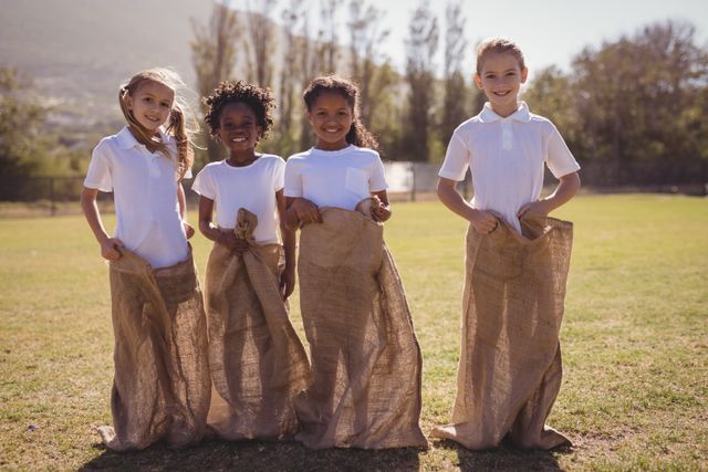 Children participating in a sack race outdoors on a sunny day. Ideal for use in educational materials, advertisements for outdoor activities, or promoting teamwork and physical exercise among kids.