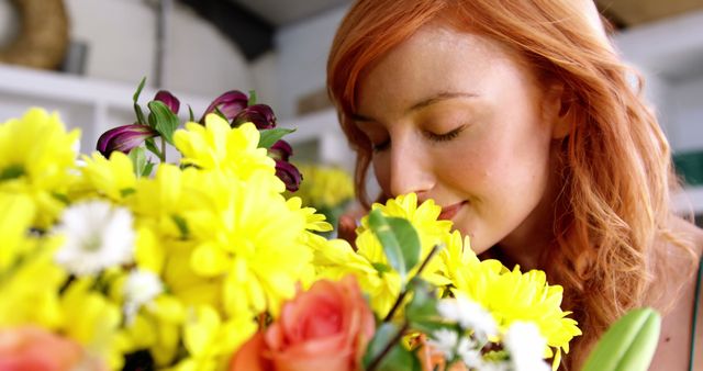 Young woman with red hair enjoying the fragrance of a bright, fresh flower bouquet. Perfect for themes of relaxation, spring, happiness, and nature. Ideal for advertisements, wellness blogs, and greeting cards.