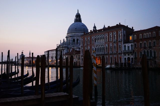 The Grand Canal in Venice at twilight showcasing illuminated historic buildings and anchored gondolas. The picturesque scene highlights the famous basilica and serene waters, perfect for travel and tourism promotions, romantic getaway advertising, and cultural heritage studies.