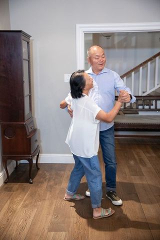 Senior asian couple dancing in home entryway on hardwood floor showing affection