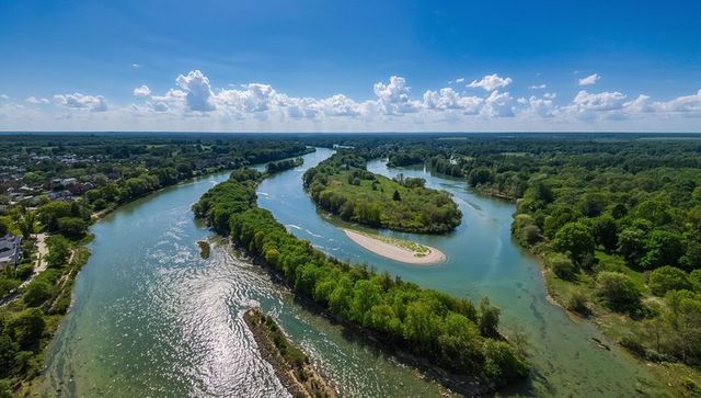 Winding river curving around treed islands and sandy spit, aerial panorama of rural valley