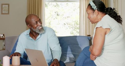 Senior african american couple talking on couch while using laptop and enjoying coffee