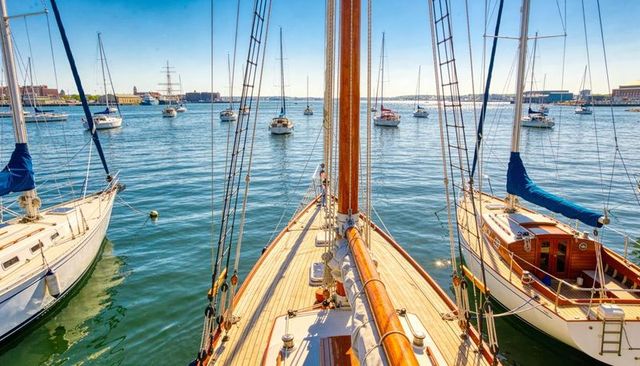 Centered wooden sailboat bow showcasing teak deck and varnished mast in sunlit marina