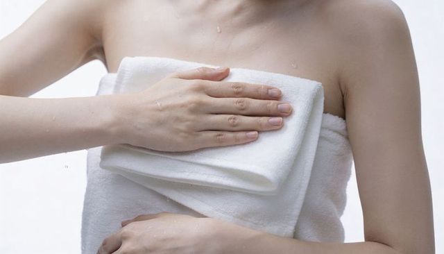 Woman wrapping white towel across wet chest in shower, close-up spa and skincare concept