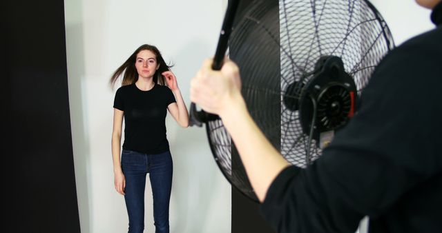 Photographer holding fan for female model during photo shoot in studio