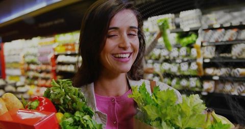 Smiling woman shopping with fresh produce and grocery bags in vibrant supermarket aisle