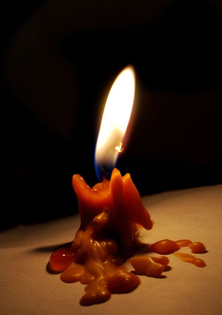 A visuals showing a close-up of a melting candle illuminating with an intense flame against a dark background. Ideal for representing themes of serenity, warmth, solitude, or symbolizing hope and reflection in various contexts. Suitable for use in wellness, relaxation or meditation related content.