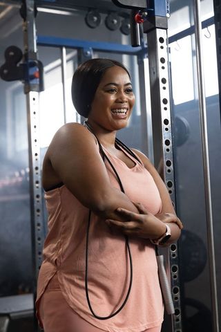 Confident african american woman smiling at gym with jump rope draping over shoulders