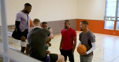 Male basketball team gathering on indoor court discussing strategy and teamwork