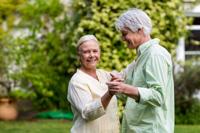 Senior couple enjoying a dance in their garden, showcasing love and happiness in their retirement years. Ideal for use in advertisements, retirement planning brochures, lifestyle blogs, and health and wellness articles focusing on active aging and relationships.