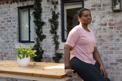 African american woman sitting on wooden patio table wearing pink tee and smartwatch
