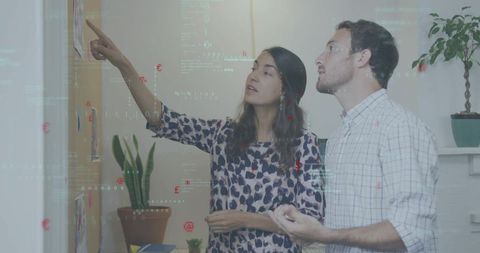 Young professionals collaborating at corkboard with sketches, data overlay and brainstorming energy