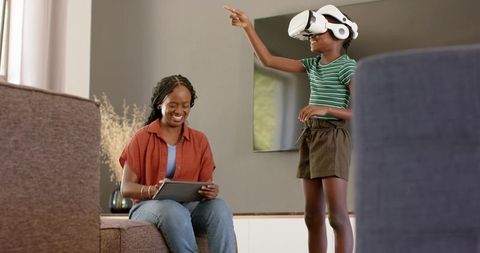 African american mother guiding child using vr headset while holding tablet in living room