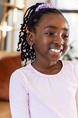 African american girl smiling in pale pink top with purple scrunchie, joyful portrait