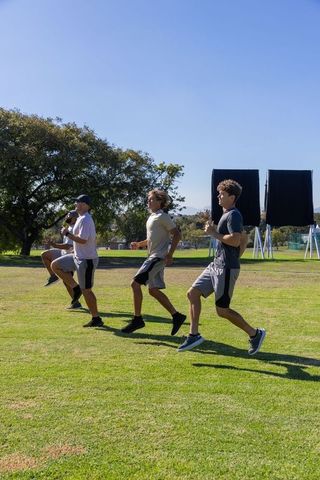 Male team performing high-knee running drill on grassy field for athletic conditioning