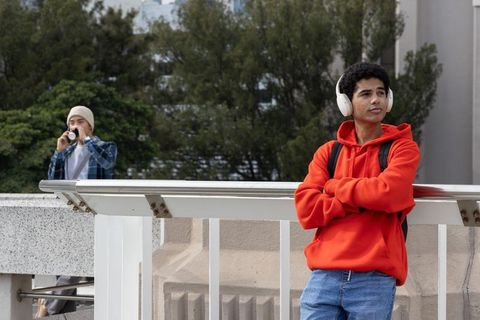 Teen in red hoodie listening to music while friend sipping coffee on urban balcony