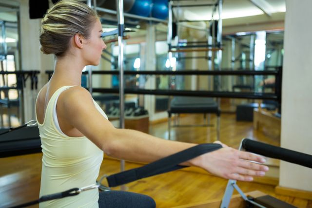 Determined woman practicing stretching exercise on reformer in gym