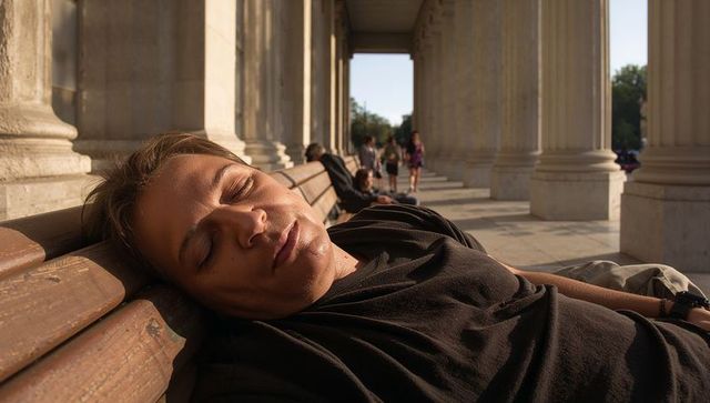 Man reclining on bench basking in warm sunlight under classical colonnade with columns