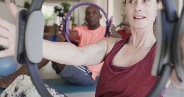 Group of older adults participating in a Pilates class, using fitness rings for core strength exercises. Ideal for illustrating fitness classes, promoting healthy lifestyles, gyms, and wellness programs.