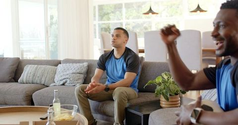 Diverse friends watching live soccer match at home with tense focus and joyful celebration