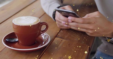 Casual cafe hands typing on smartphone with beaded bracelet beside latte art cup on table