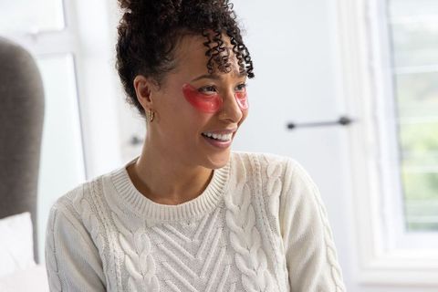 African american woman wearing pink under-eye gel patches smiling in cozy cable knit sweater