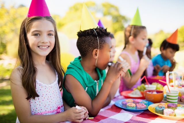 Group of kids enjoying a birthday party in a park. Ideal for themes related to childhood joy, outdoor activities, festive events, and children's celebrations. Suitable for use in promotions for party planning, family-oriented events, and child care services.