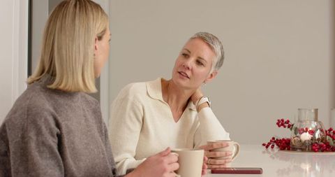 Two women chatting over coffee in minimal kitchen with neutral tones and holiday candles