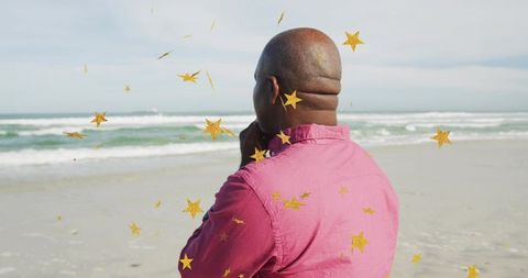 Senior Man Contemplating Ocean on Sandy Beach with Gold Star Confetti