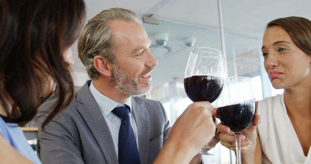Three colleagues, two women and one man, are toasting with red wine in a corporate event. They are dressed in formal attire, highlighting a professional yet joyous atmosphere. This image is perfect for illustrating team bonding, corporate celebrations, office parties, and business-related events.