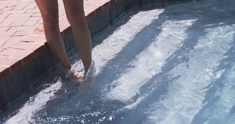 Female standing on pool step with sunlit water ripples, backyard summer relaxation