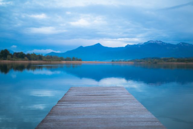 Perfect for uses in travel brochures, nature websites, inspiration for outdoor activities, or peaceful scene backgrounds. The wooden pier leading to still waters with a majestic mountain backdrop gives a sense of calm and beauty.