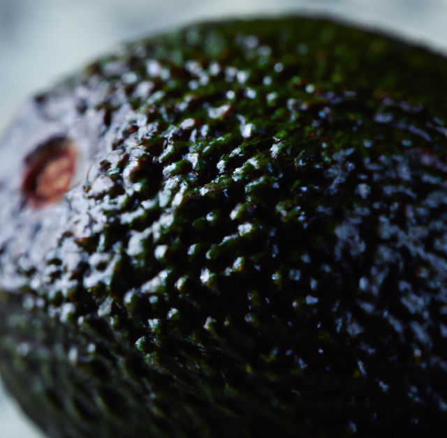 Close-up image highlighting the detailed texture of a ripe avocado. The rough, bumpy surface is displayed in sharp focus, emphasizing its natural freshness and organic quality. Perfect for use in food blogs, health and nutrition articles, supermarket advertising, or any content promoting healthy eating and organic produce.