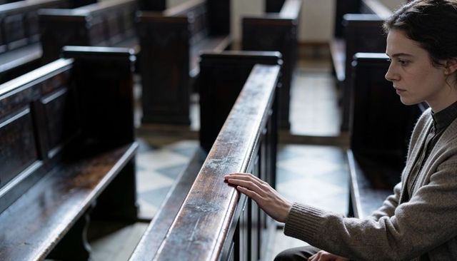 Contemplative woman sitting alone on church pew resting hand on rail interior portrait