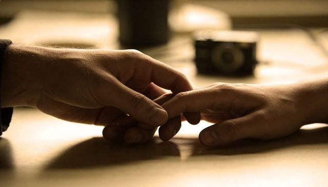 Hands interlacing on warm-lit table, romantic touch with vintage camera bokeh, sepia