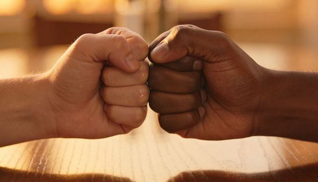 Fist-bumping friendship close-up two men knuckle touching warm golden cafe light