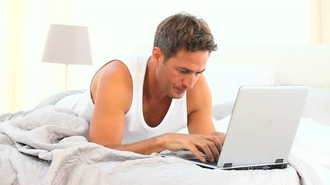Man Using Laptop While Lying in Bed Relaxed Ambiance
