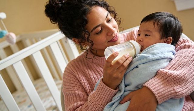 Mother feeding swaddled baby with bottle in cozy nursery, bonding moment