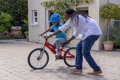 African american father teaching son to ride bike on driveway wearing helmet outdoor safety lesson