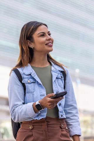 Confident african american woman using smartphone wearing denim jacket smartwatch and backpack